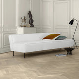 A low white fabric sofa on thin black legs in a panelled room with a herringbone wood floor