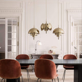 Three brass dome pendants with tiered inner shades hang over a dark table and rust velvet chairs