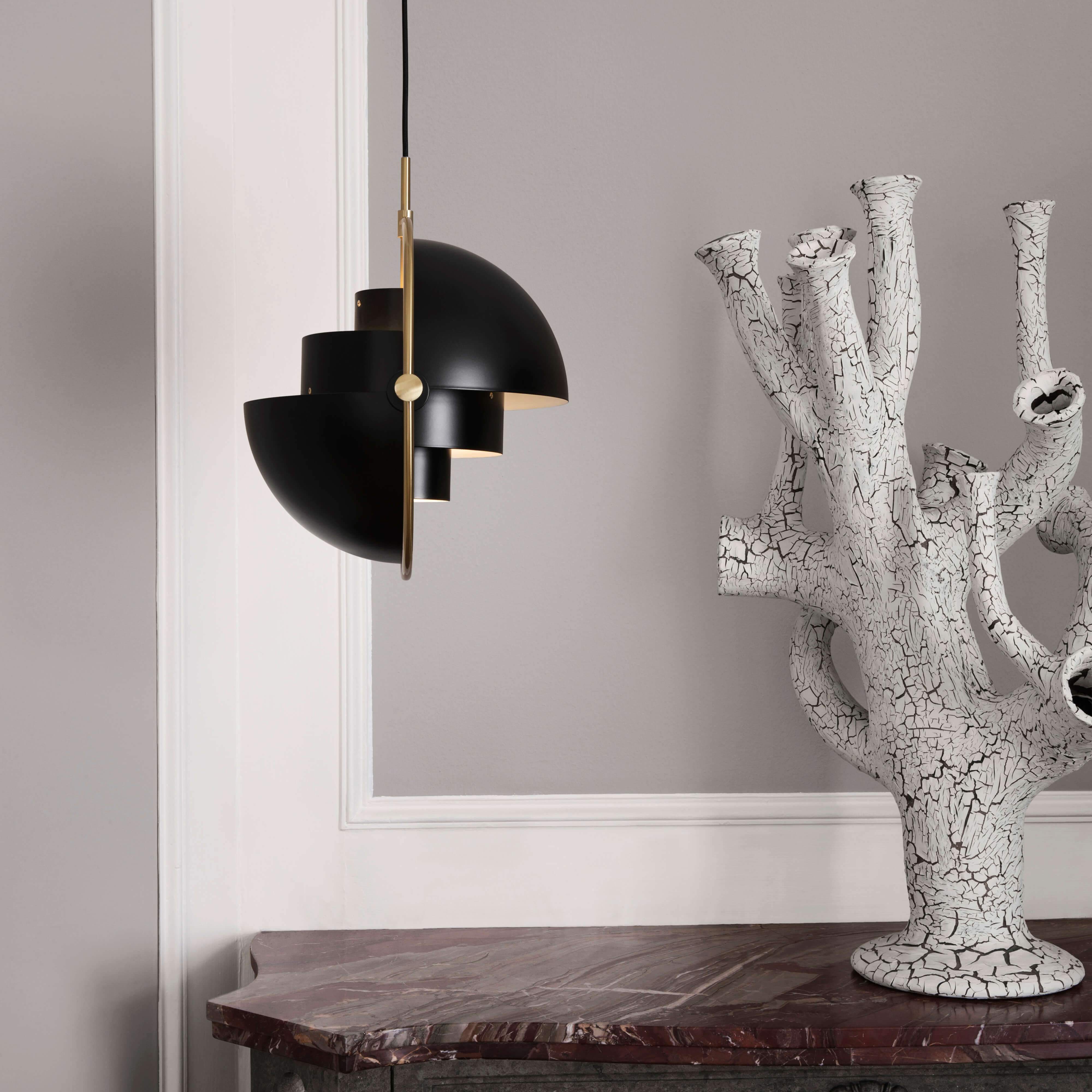 A black pendant light with layered half-dome shades and a brass arm, beside a cracked white ceramic sculpture