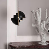 A black pendant light with layered half-dome shades and a brass arm, beside a cracked white ceramic sculpture