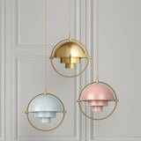 Three domed pendant lights in brass, pale blue and soft pink, each in a thin brass ring, hang before a panelled grey wall