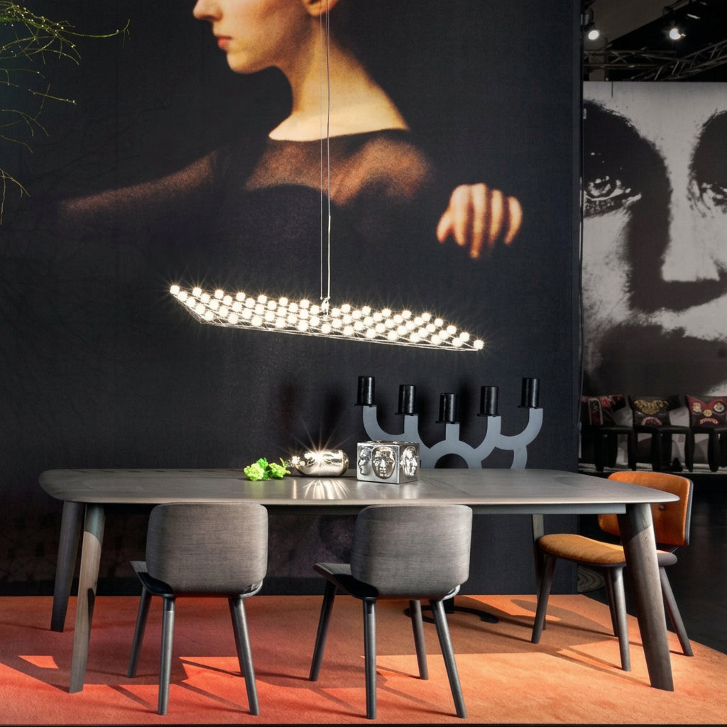 Grey fabric dining chairs on slim dark legs at a grey table, with a lit pendant above