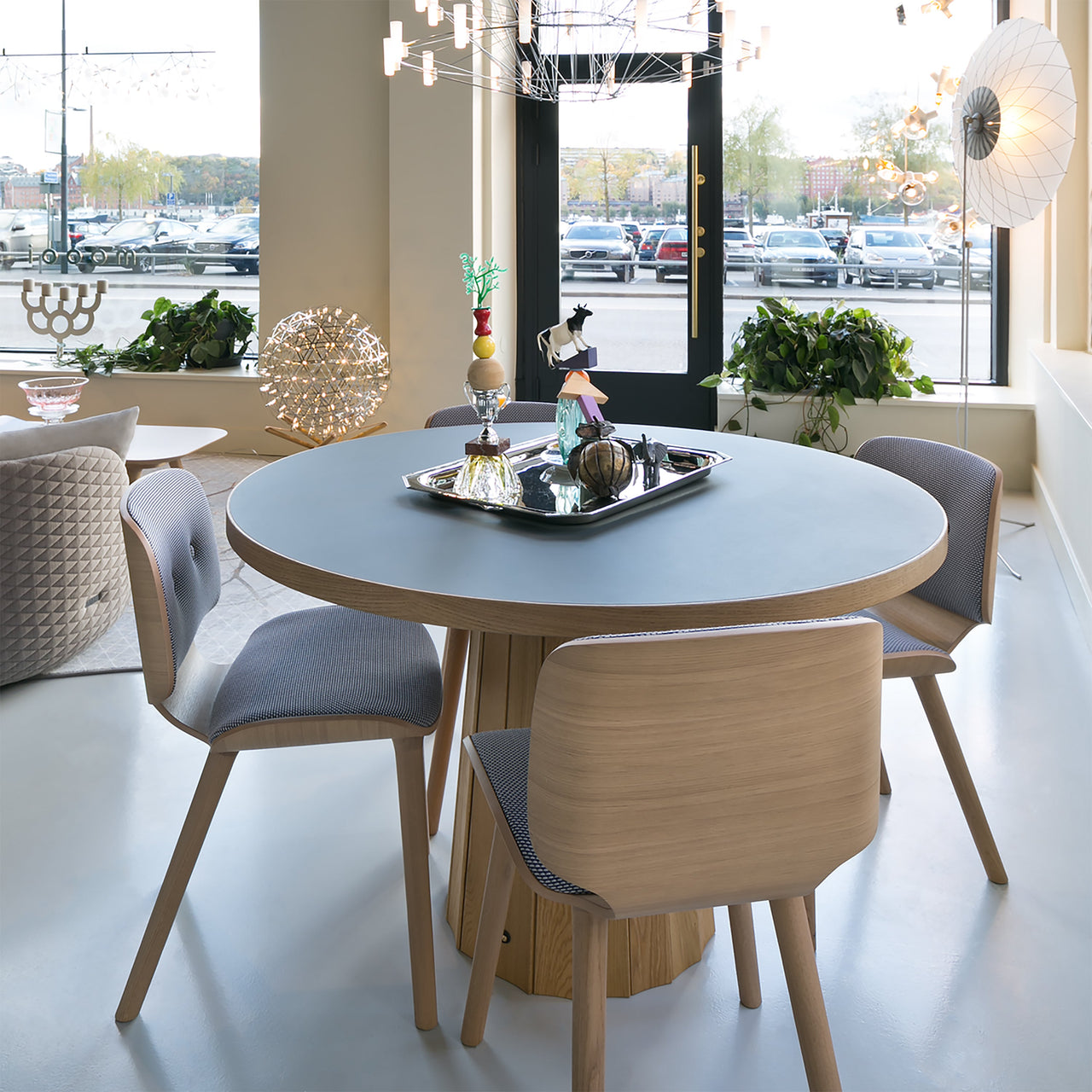 Light oak dining chairs with grey patterned seats around a round table in a bright showroom