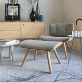 A footstool with a grey-green fabric cushion on four light wood legs, in front of a matching lounge chair